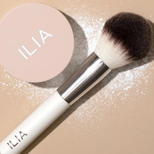 ILIA Finishing Powder Brush mit Puder vor hellem Hintergrund