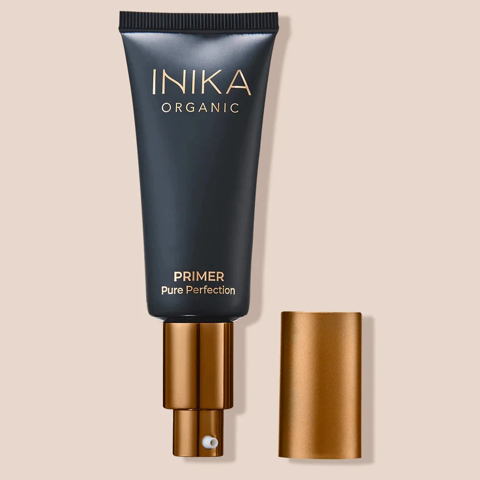 INIKA Pure Perfection Primer in schwarzer Tube und bronzefarbenen Deckel auf beigem Hintergrund North Glow