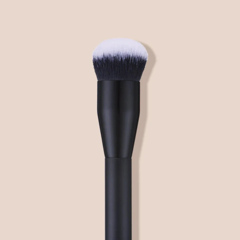 INIKA Foundation Brush mit schwarzem Griff und bronzefarbener Schrift mit schwarzen. oben weißen Borsten.