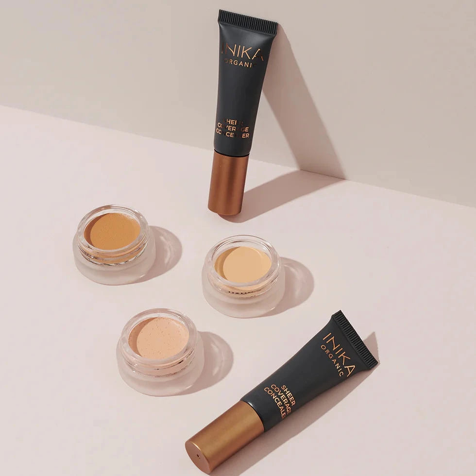 INIKA Sheer Coverage Concealer vor beigem Hintergrund mit kleinen Dosen mt Concealer, die die Farben demonstrieren