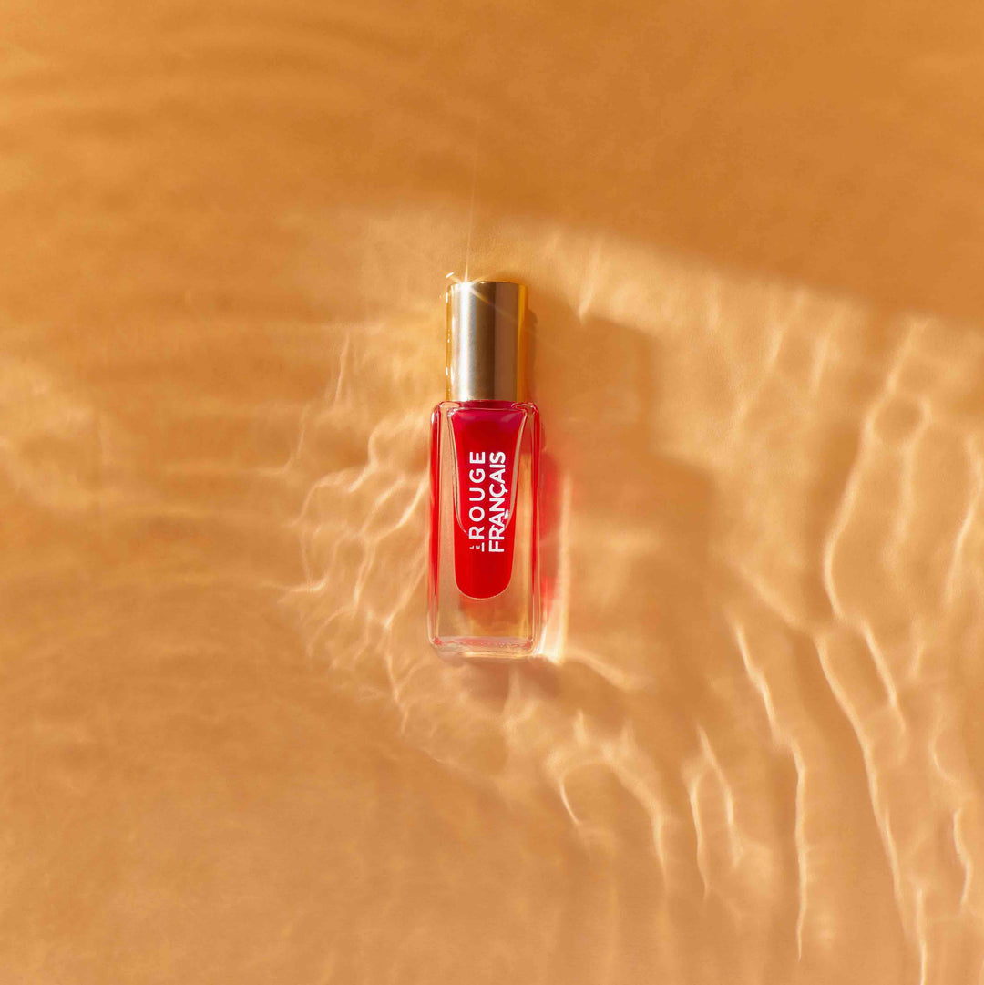 Lippenöl in einer Glasflasche ohne Deckel Le Rouge Francais liegt im seichten Wasser mit orangefarbenem Untergrund. North Glow