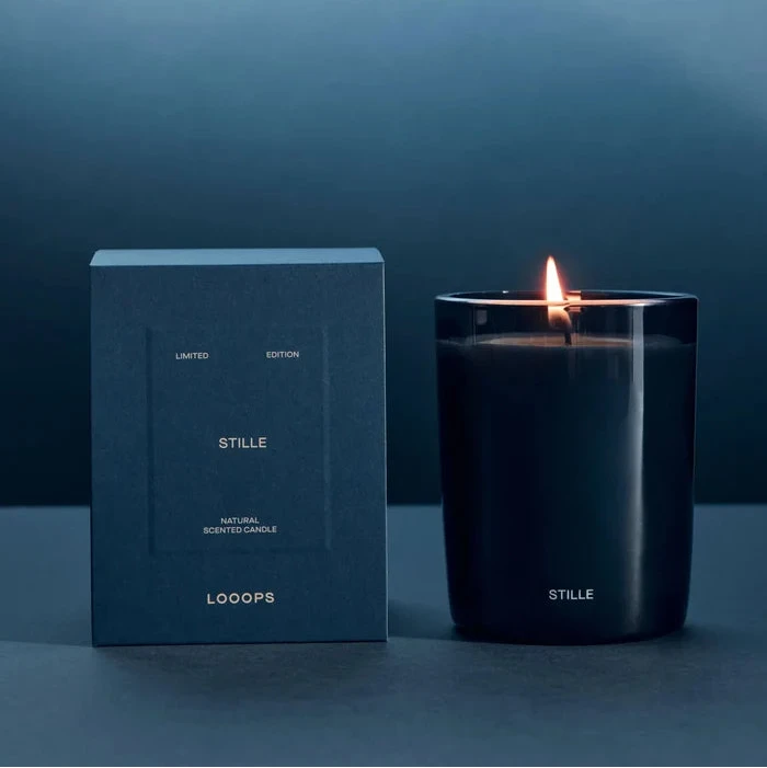 Looops Stille Kerze in blau getöntem Glas, 250 g neben Produktverpackung.