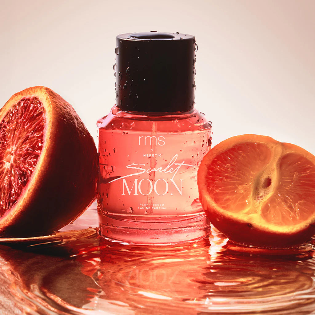 Rote RMS und X Heretic Scarlet Moon Parfum Flasche mit schwarzem Deckel steht in einer rotorangefarbenem Flüssigkeit zwischen Orangen- und Blutorangenhälften. North Glow