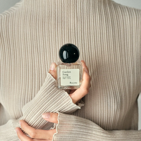 Garden Song Eau de Parfum von Racyne in einer Hand vor hellem Strickpullover