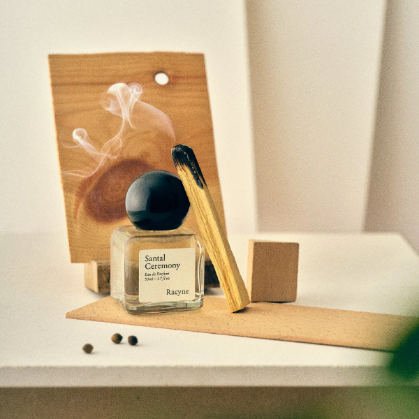 Santal Ceremony von Racyne – minimalistischer Eau-de-Parfum-Flakon in atmosphärischer Produktaufnahme mit Räucherstäbchen.