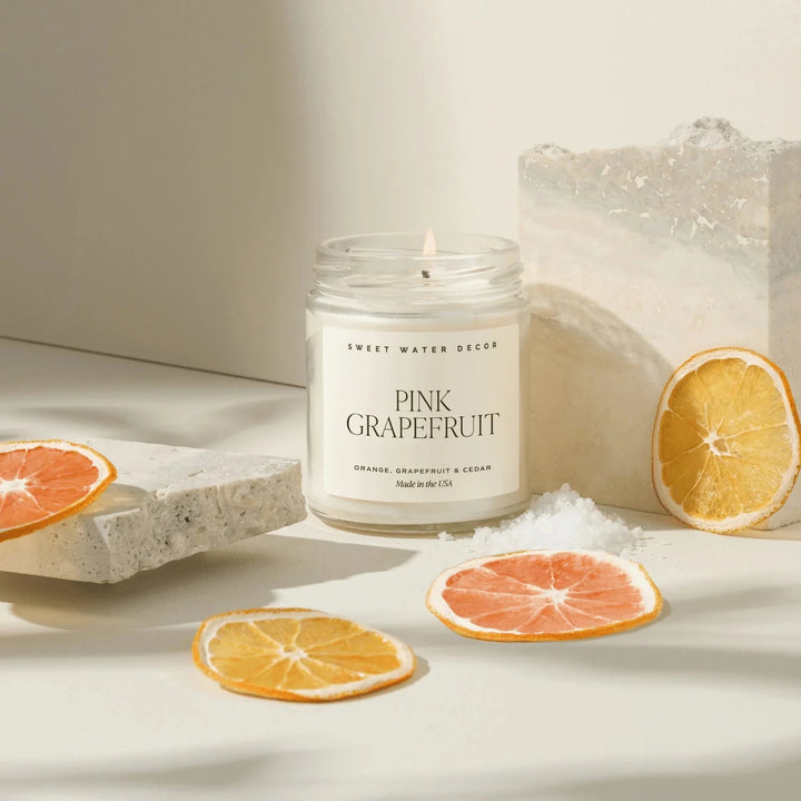 Brennende Kerze "PINK GRAPEFRUIT" von Sweet Water Decor, umegben von Orangen- und Grapefruitscheiben.