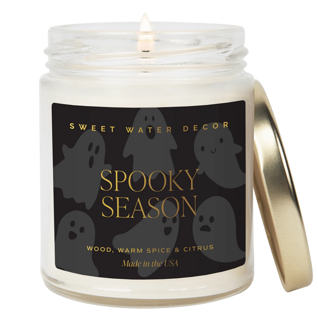 Brennende Kerze "Spooky Season" von Sweet Water Decor, daneben angelehnt ein goldener Deckel vor weißem Hintergrund. North Glow