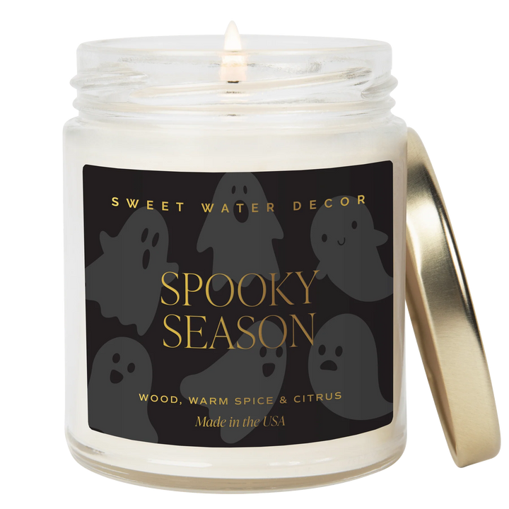 Brennende Kerze "Spooky Season" von Sweet Water Decor, daneben angelehnt ein goldener Deckel vor weißem Hintergrund.