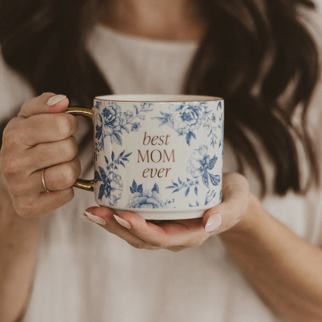 Kaffee-/Teetasse mit blauem Delfter Muster mit goldener Schrift best MOM ever und goldenem Henkel mit von zwei Händen gehalten. North Glow