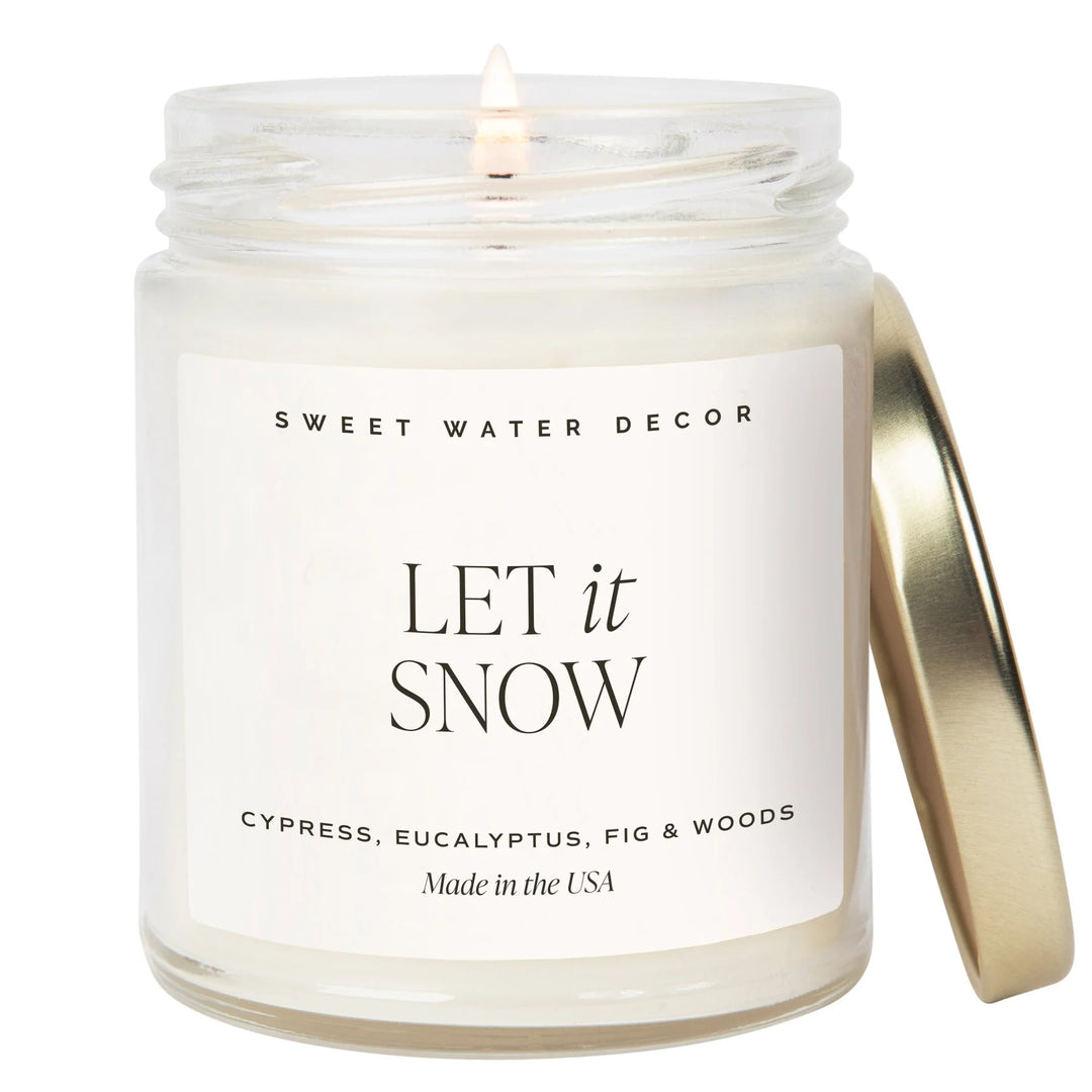 Brennende Kerze in einem Kerzenglas mit Aufschrift "LET it SNOW" von Sweet Water Decor, daneben angelehnt ein goldener Schraubdeckel. North Glow