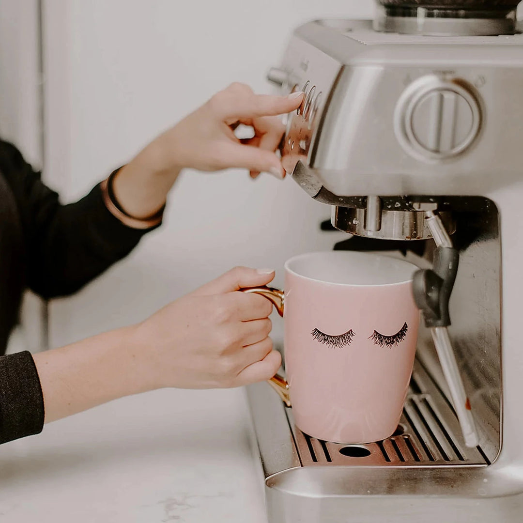 Frau hält Kaffeetasse "Pink Eyelashes" unter eine Siebträgermaschine