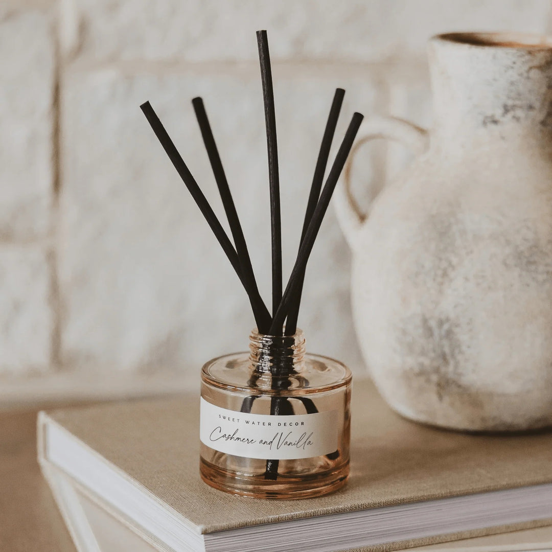 Diffuser Cashmere and Vanilla Tinted Glass Jar mit Duftstäbchen steht auf einem Buch. North Glow
