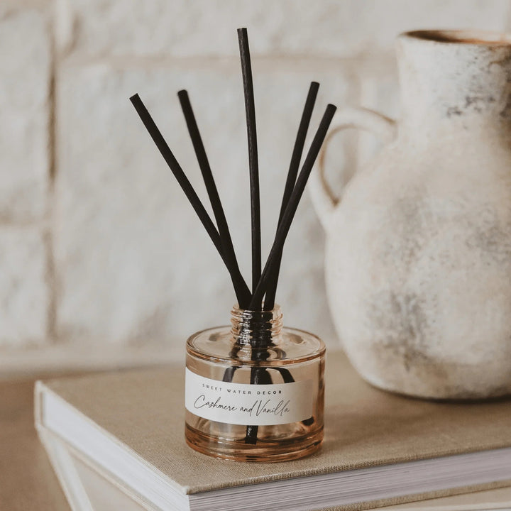 Diffuser Cashmere and Vanilla Tinted Glass Jar mit Duftstäbchen steht auf einem Buch.