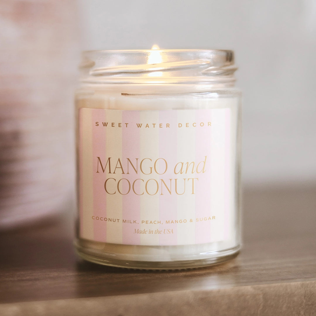Brennende Sojawachskerze Mango and Coconut steht auf einer hölzernen Unterlage.
