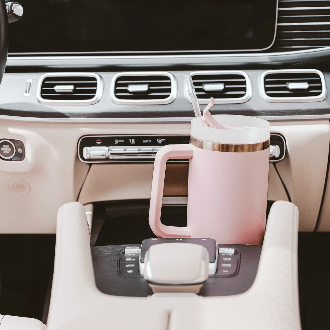 RosafarbenerTumbler / Thermobecher von Sweet Water Decor steht in der Mittelkonsole eines Autos. North Glow