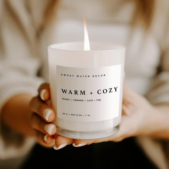 2 Hände halten Brennende Sojawachskerze Sweet Water Decor Warm + Cosy im Milchglas.