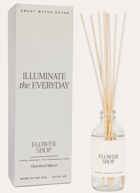 Transparente Flasche Raumduft Flower Shop Sweet Water Decor mit Schilfrohrstangen steht neben der Verpackung vor hellem Hintergrund. North Glow