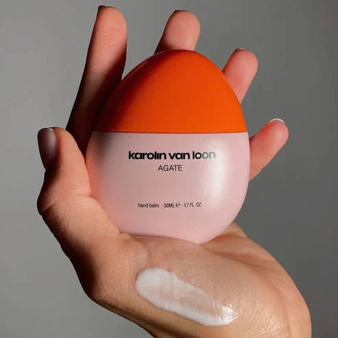 Frauenhand hält elegante Handlotion-Flasche mit korallenrosa Verschluss, feine Hauttextur und cremige Lotion deutlich sichtbar