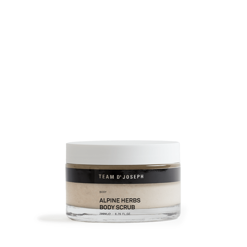 Team Dr Joseph Alpine Herbs Body Scrub – eleganter Glastiegel mit weißem Deckel und schwarzem Etikett, naturfarbenes Körperpeeling sichtbar durch das transparente Glas.