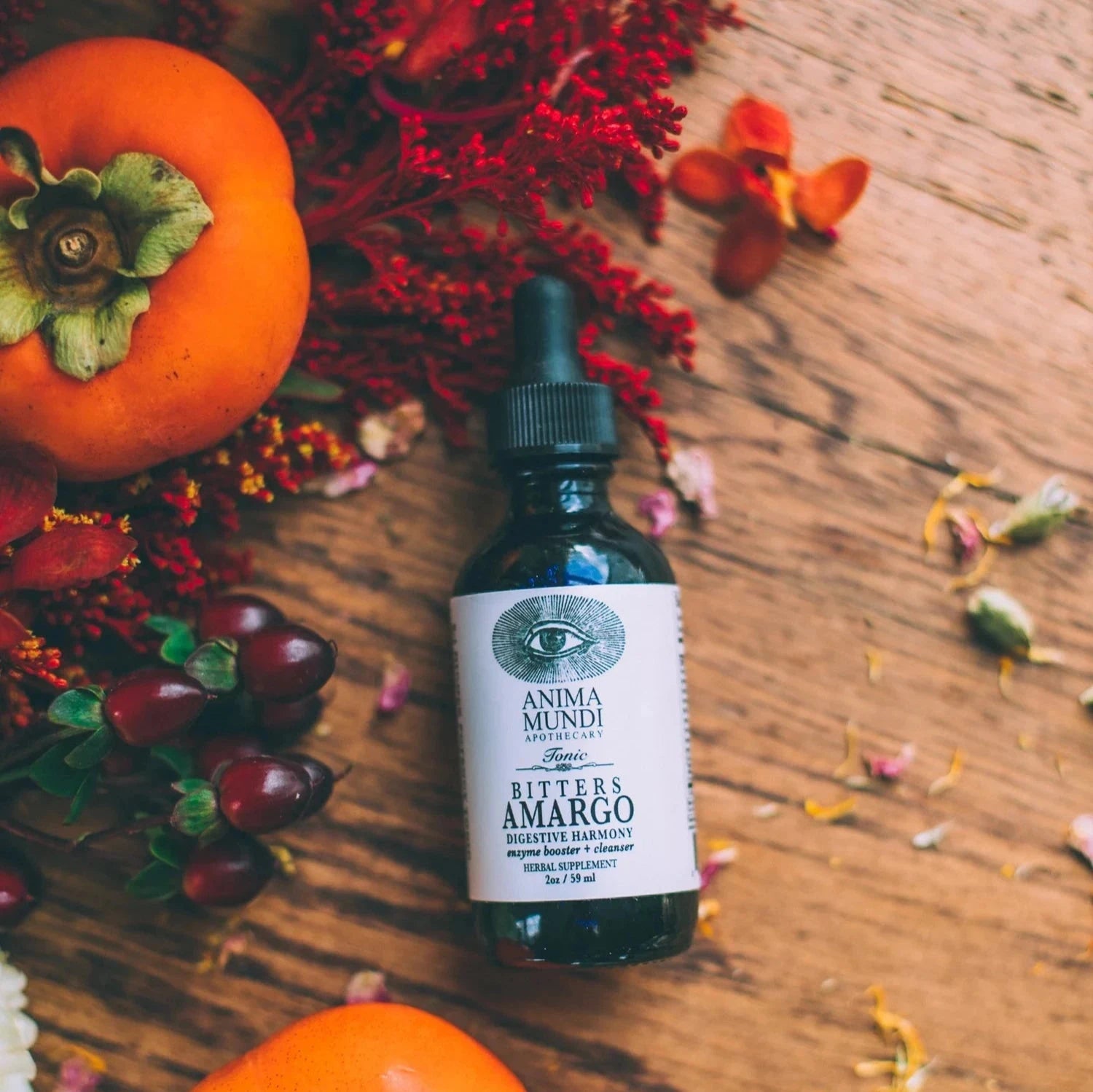 Anima Mundi Pipettenglasflasche Amargo liegt auf einem Holztisch dekoriert mit getrockneten Blumen, Kräutern und Beeren.