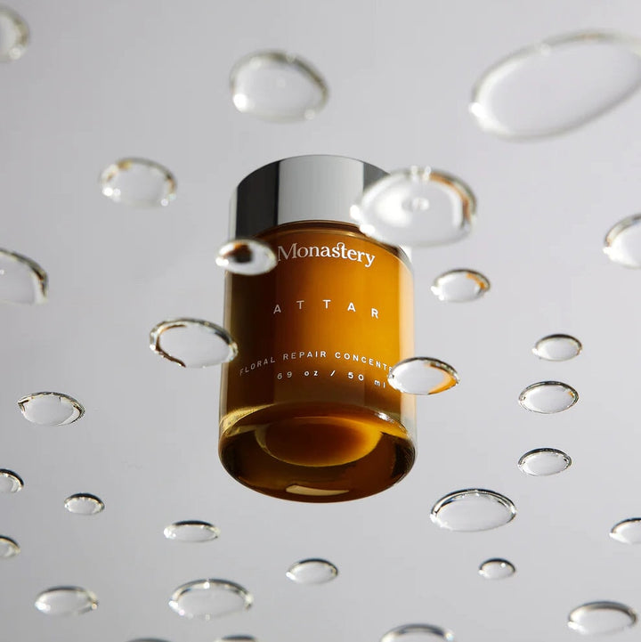 Monastery Attar Balm Konzentrat 50ml Tiegel durch transparenter Scheibe mit Wassertropfen fotografiert.