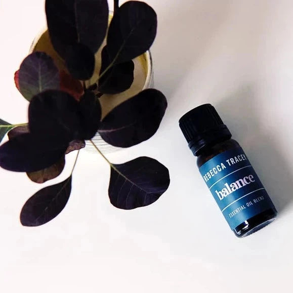 Rebecca Tracey Essential Oil auf weißem Untergrund neben dunkler Blume