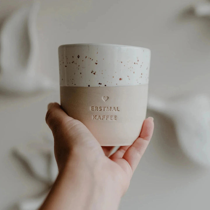 Kaffeetasse mit Prägung "Erstmal Kaffee" von Eulenschnitt wird in einer Hand gehalten.