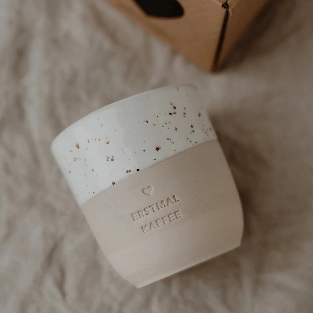 Tasse mit Prägung "Erstmal Kaffee" von Eulenschnitt liegt auf einem beigen Leinentuch. North Glow
