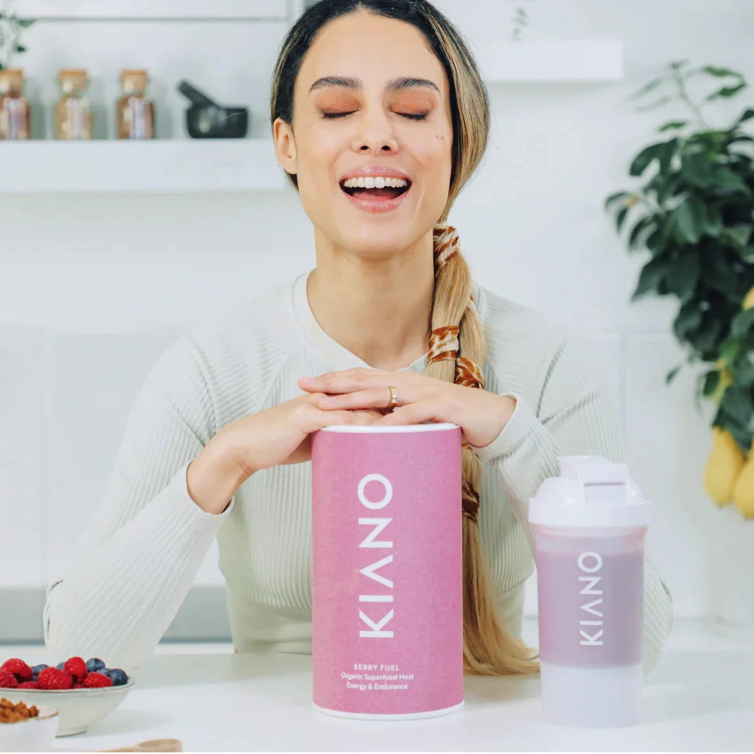 Frau sitzt mit geschlossenen Augen und lächelnd am Tisch und hat ihre Hände auf eine Dose Berry Fuel gelegt