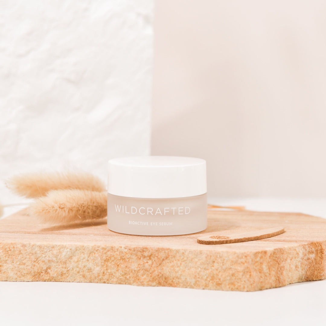 Milchglastiegel mit weißem Deckel Wildcrafted Bioactive Eye Serum steht auf einer cremefarbenen Steinplatte. North Glow