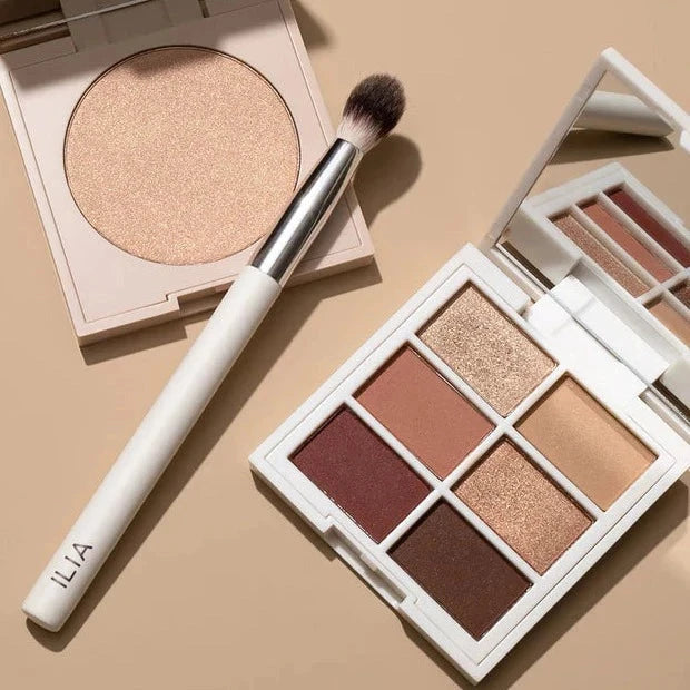 Ilia Blending Brush mit Highlighter und Lidschatenpalette vor beigen Hintergrund