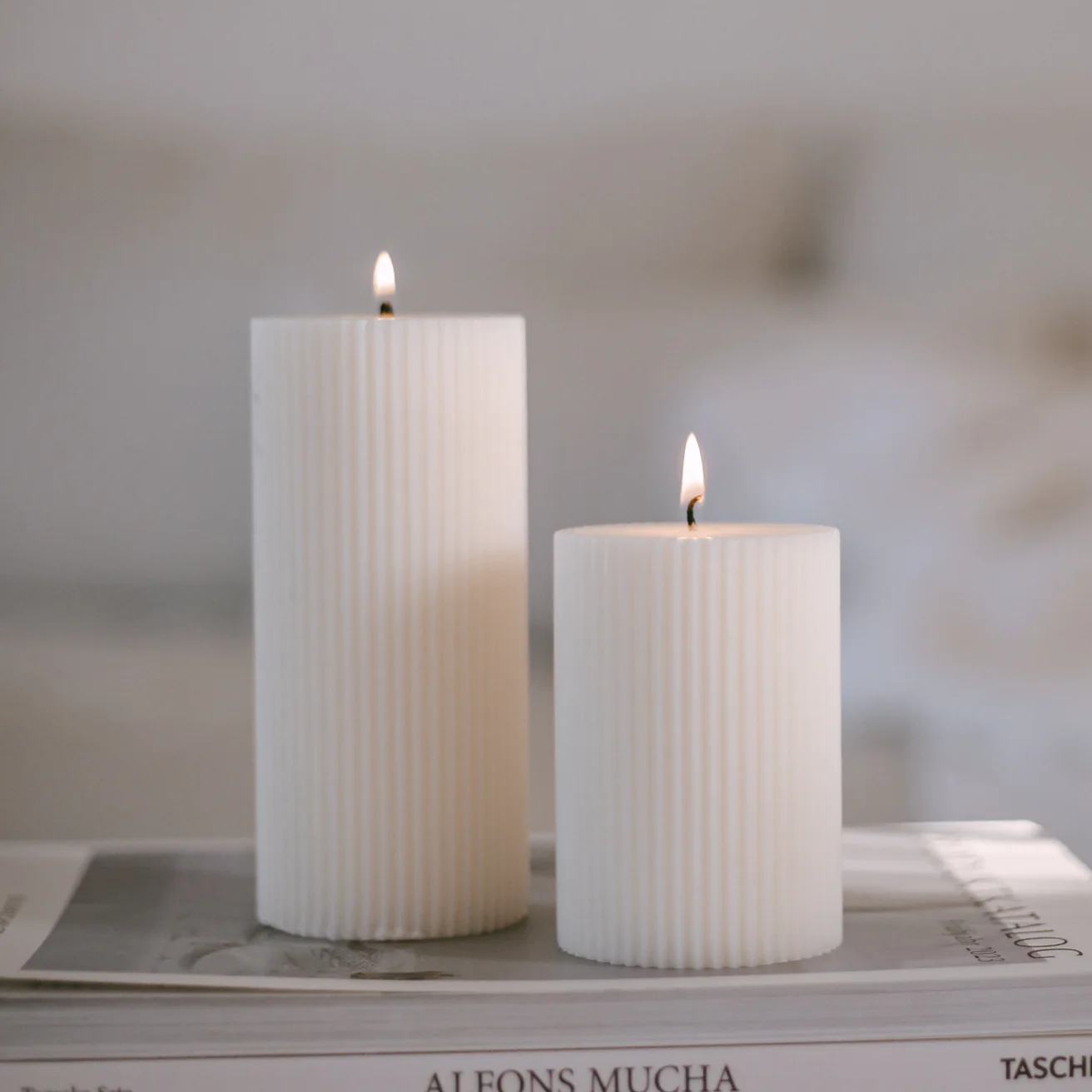 2 verschieden große Blockkerzen Rillen von Eulenschnitt in weiß stehen auf Produktkatalogen.