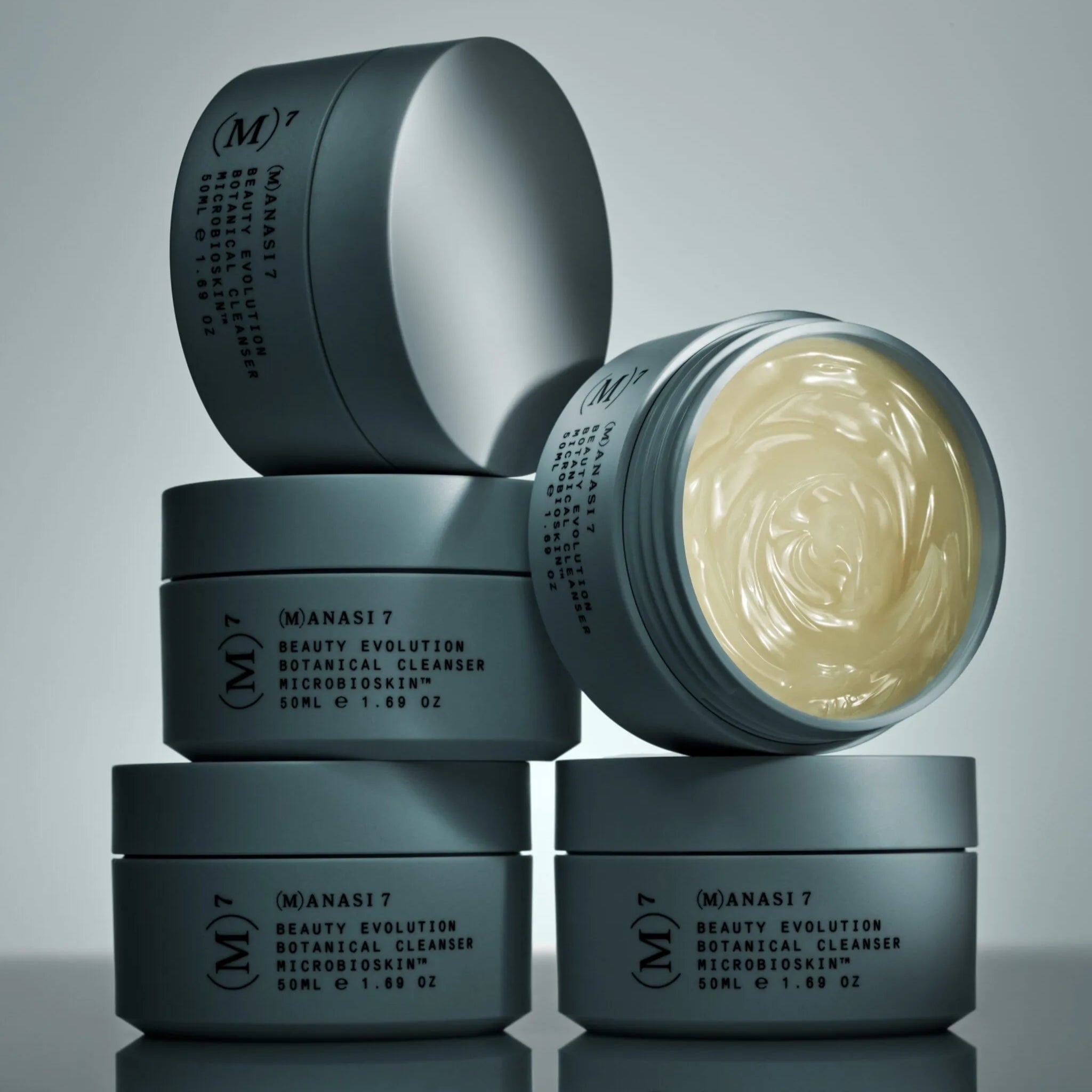 Offener Tiegel der Manasi 7 Botanical Face Cream Furora steht auf mehreren geschlossenen Tiegeln vor dunklem Hintergrund.