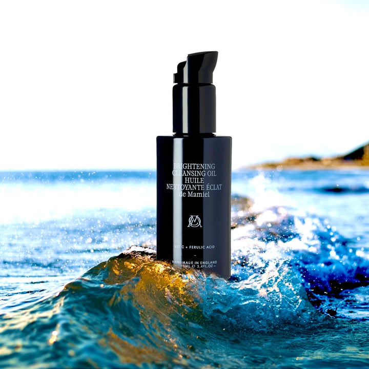 Schwarze Glasflasche  Brightening Cleansing Oil steht im Meer