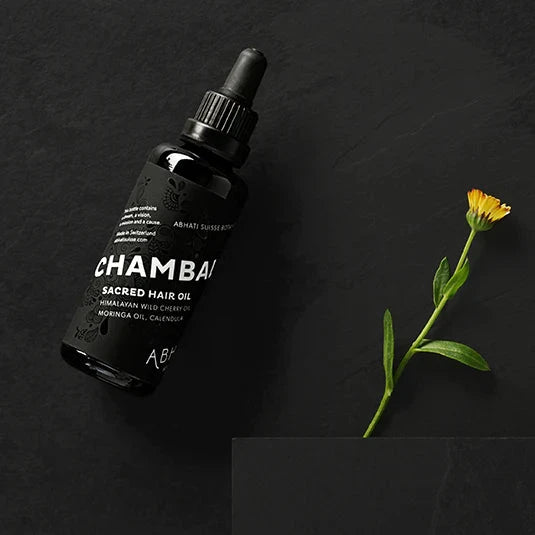 Schwarze Glaspipettenflasche Abhati Suisse Chambal Hair Oil liegt auf schwarzem Untergrund. North Glow