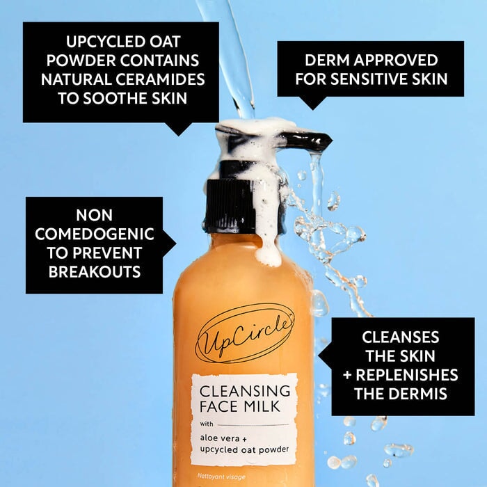 UpCircle Cleansing Face Milk mit Aloe Vera und upgecyceltem Haferpulver – milchige Textur in Glasflasche mit schwarzem Pumpkopf, umgeben von Wassertropfen auf blauem Hintergrund.
