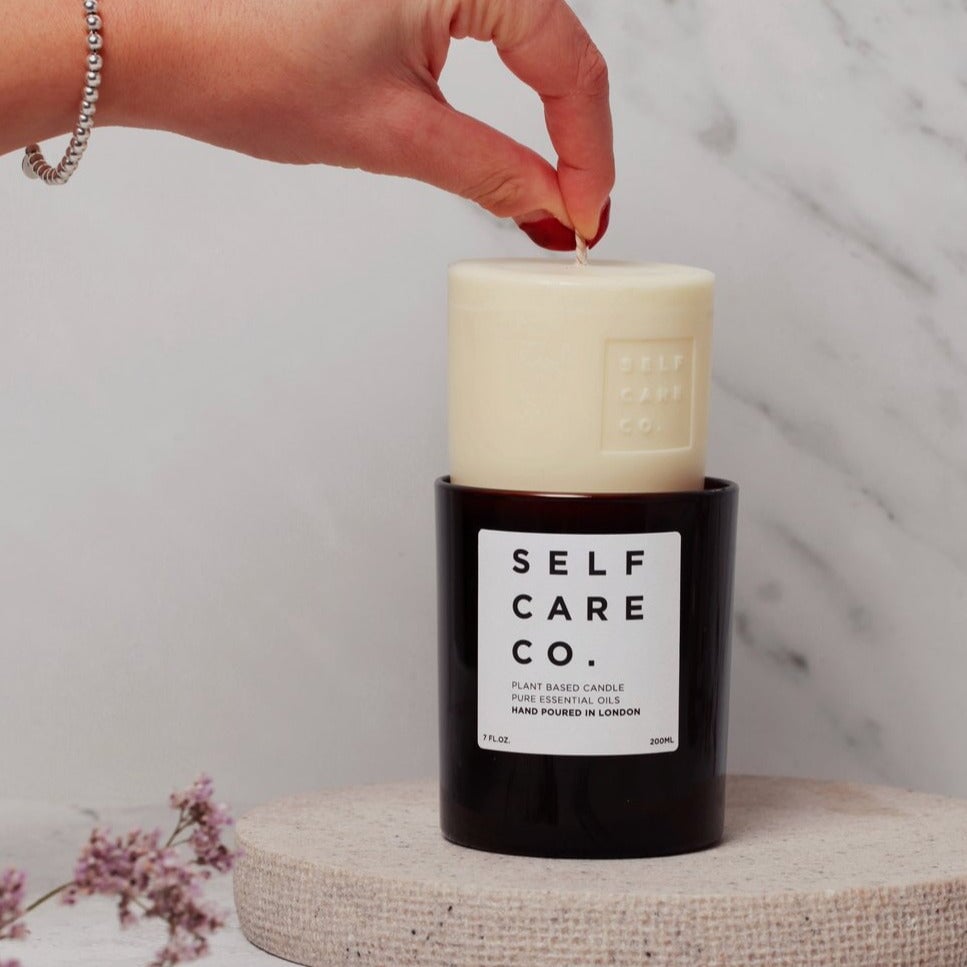 Frauenhand hält eine Kerze am Docht und lässt sie in das braune Kerzenglas von Self Care Co. gleiten