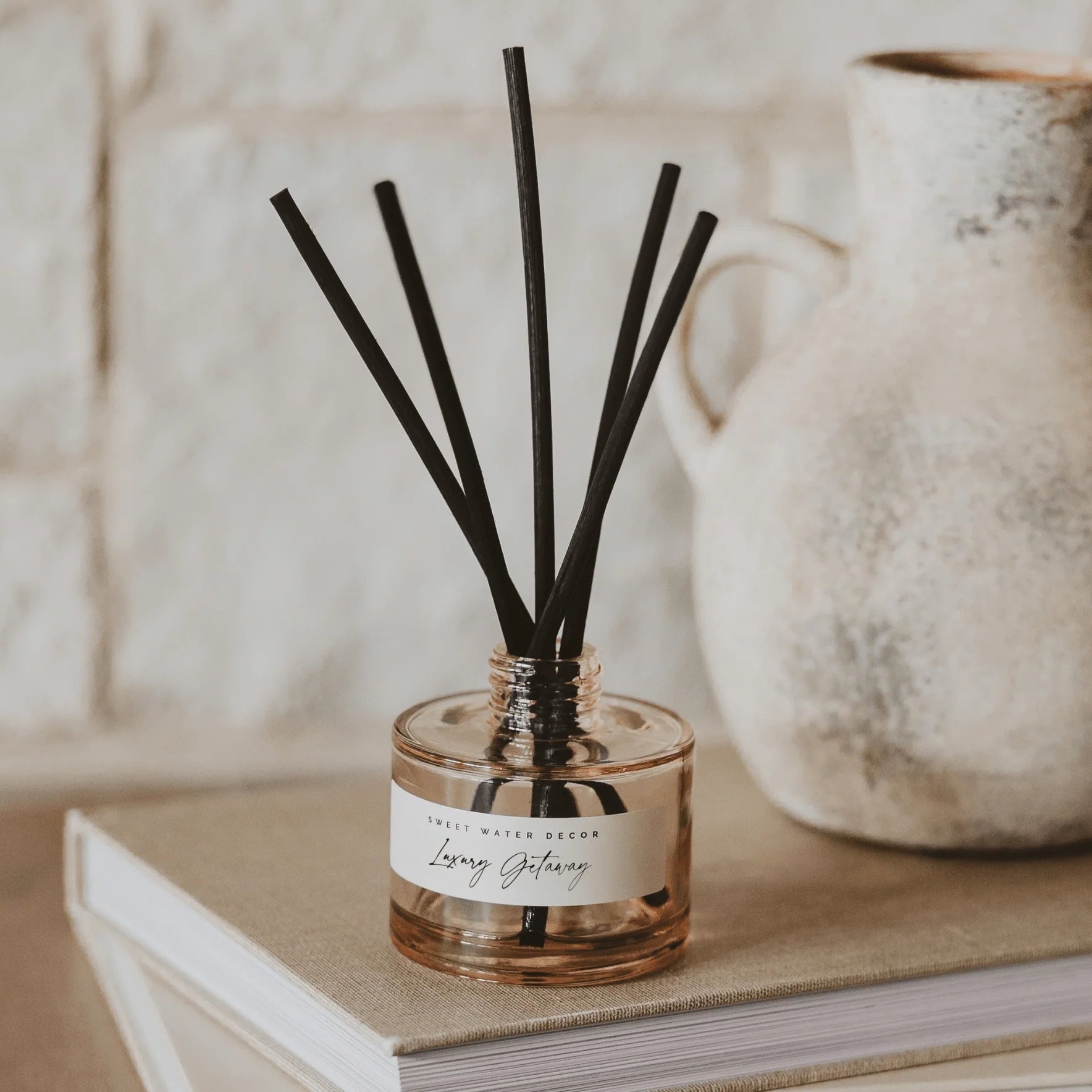 Diffuser Luxury Getaway Tinted Glass Jar mit Duftstäbchen steht auf einem Buch.