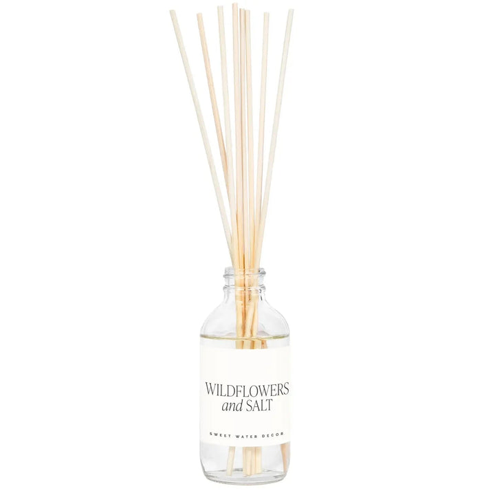 Transparente Flasche Diffuser Wildflowers and Salt von Sweet Water Decor mit Schilfrohrstangen, steht vor hellem Hintergrund.