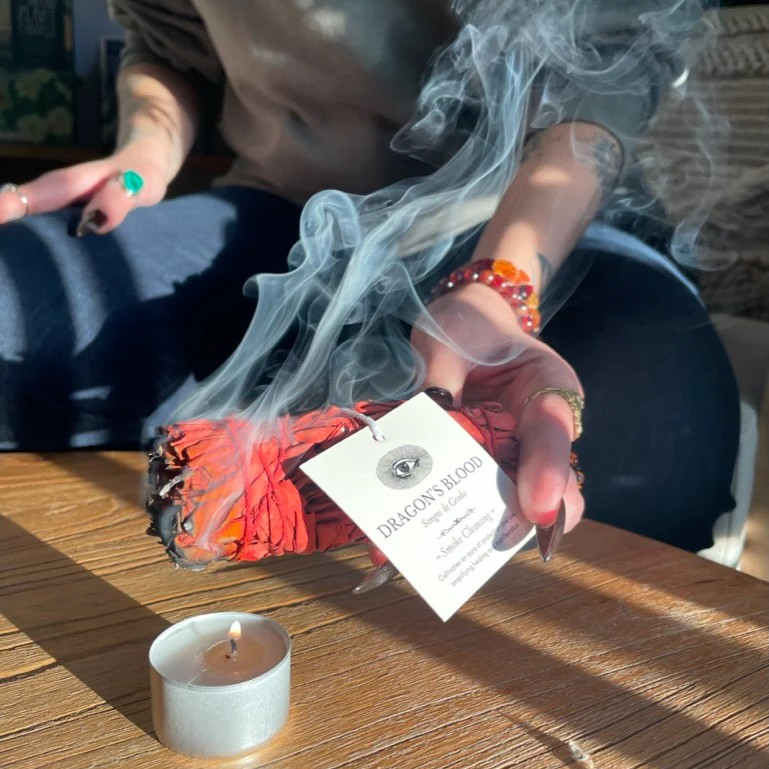 Dragon’s Blood Wand aus weißem Salbei, mit rotem Harz umhüllt, wird über einer Kerze entzündet North Glow