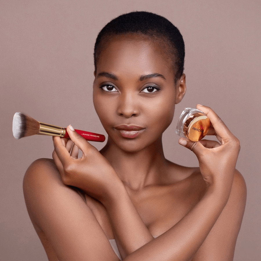 Frau hält in einer Hand Puder Pinsel Le Rouge Francais Dual-Fiber Powder Brush, in der anderen einen Puder Tiegel.
