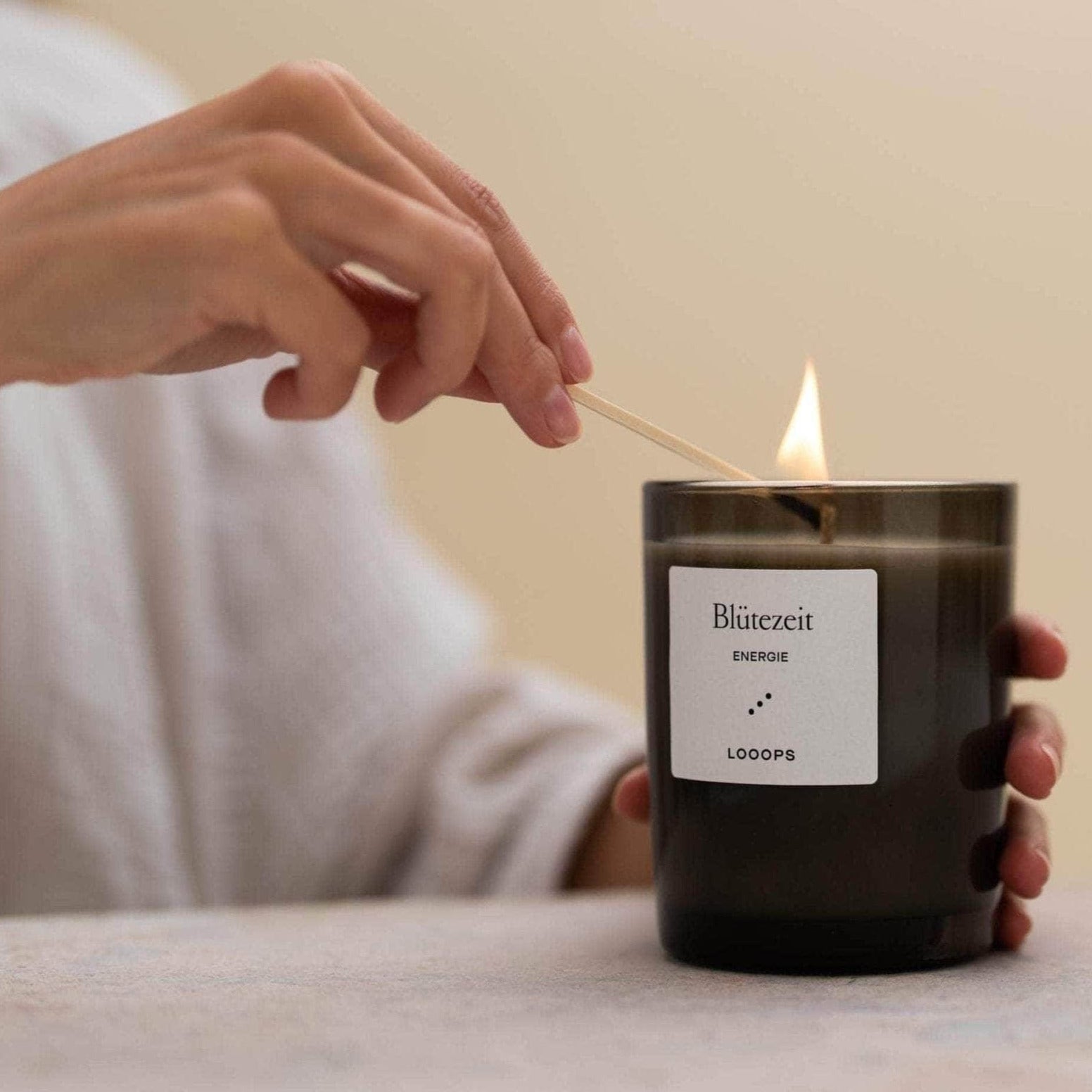 Kerze in braunem KErzenglas wird von einem Streichholz von Looops angezündet.