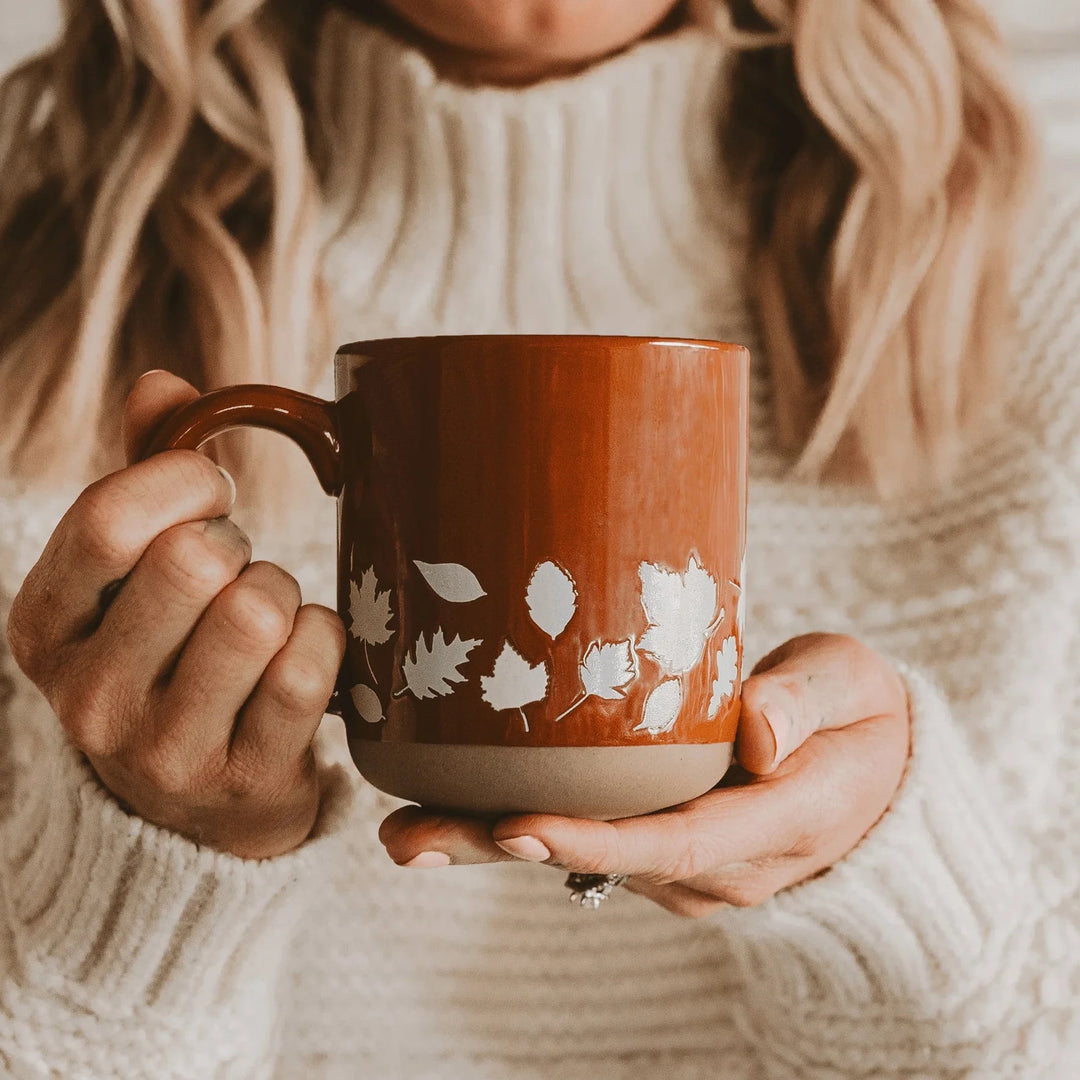 Fall Leaves orangene Kaffeetasse von Sweet Water Decor wir von zwei Händen in die Kamera gehalten.