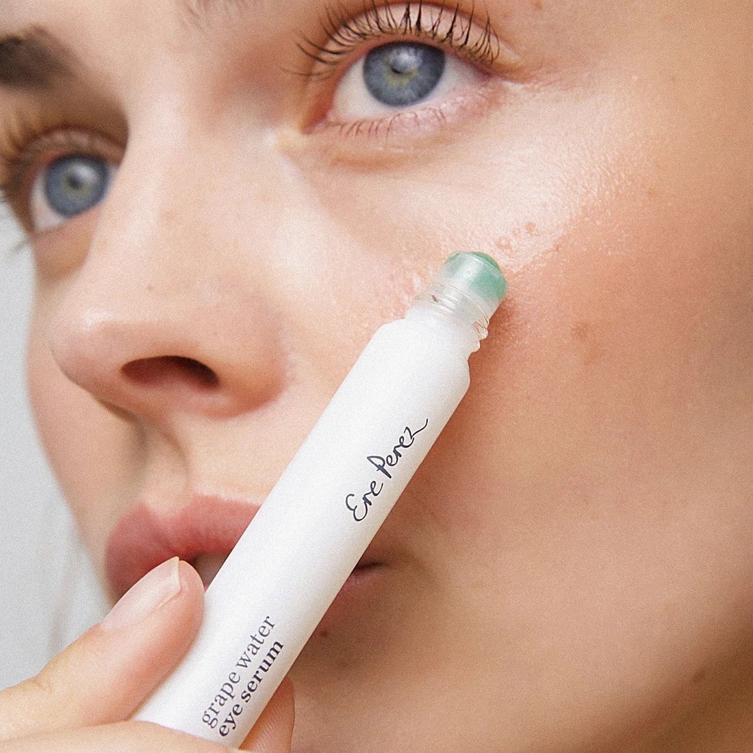 Frau trägt das Ere Perez Grape Water Eye Serum mit Jade-Roller sanft unter dem Auge auf
