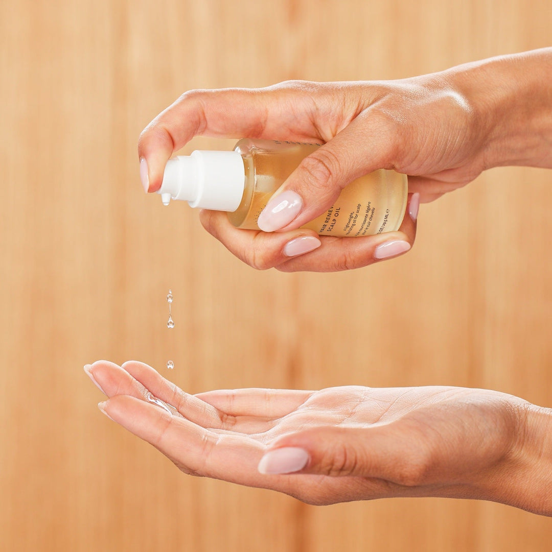 Eine Hand hält eine Hair Renew Scalp Oil Flasche waagerecht und spritzt ein paar Öltropfen auf die andere Hand. North Glow