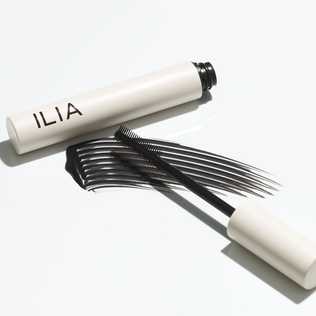 Textur- und Farbbeispiel der Ilia Limitless Lash Mascara mit  offener Mascara und danebenliegender Bürste. North Glow