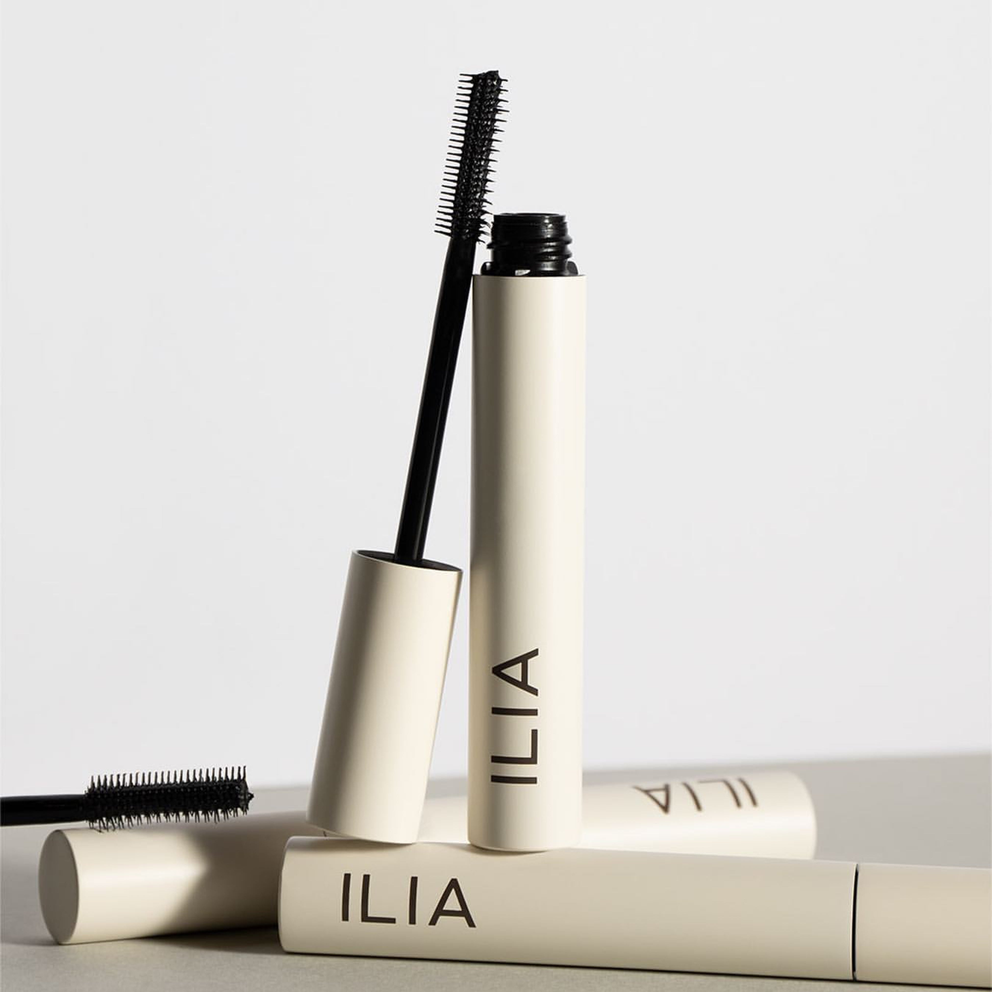 Offene Ilia Mascara mit angelehnter Bürste steht auf einer geschlossenen Mascara.