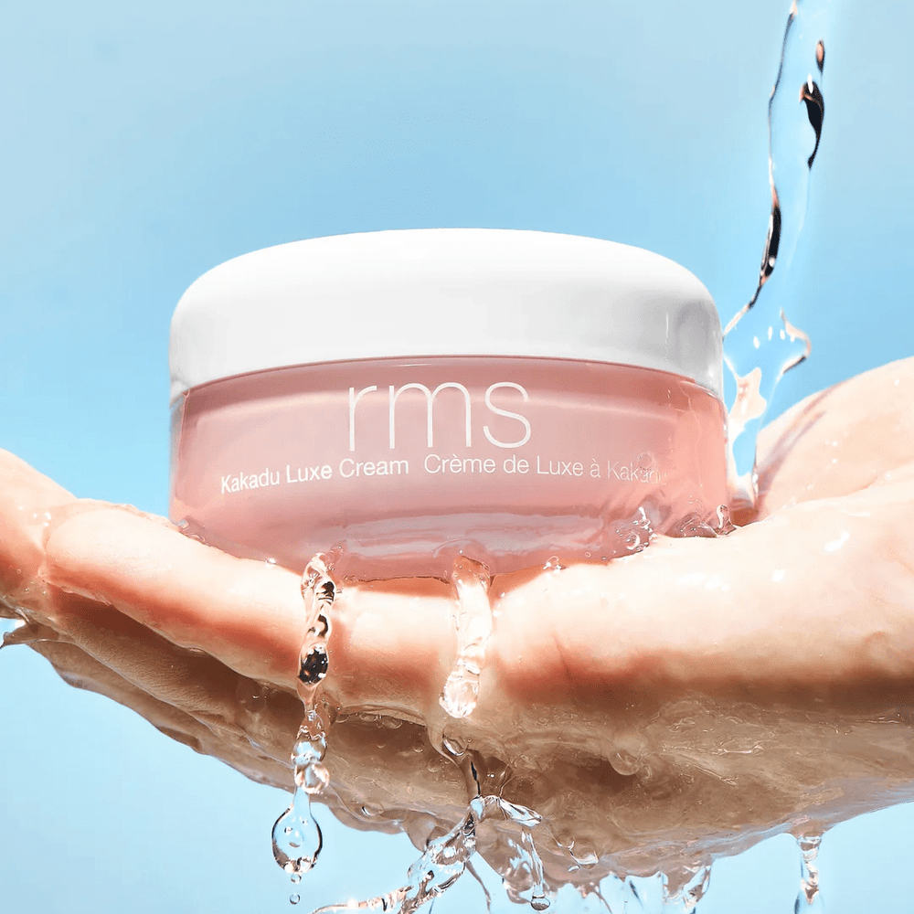 Cremedose der Kakadu Luxe Cream von RMS Beauty auf einer Hand, über die Wasser fließt