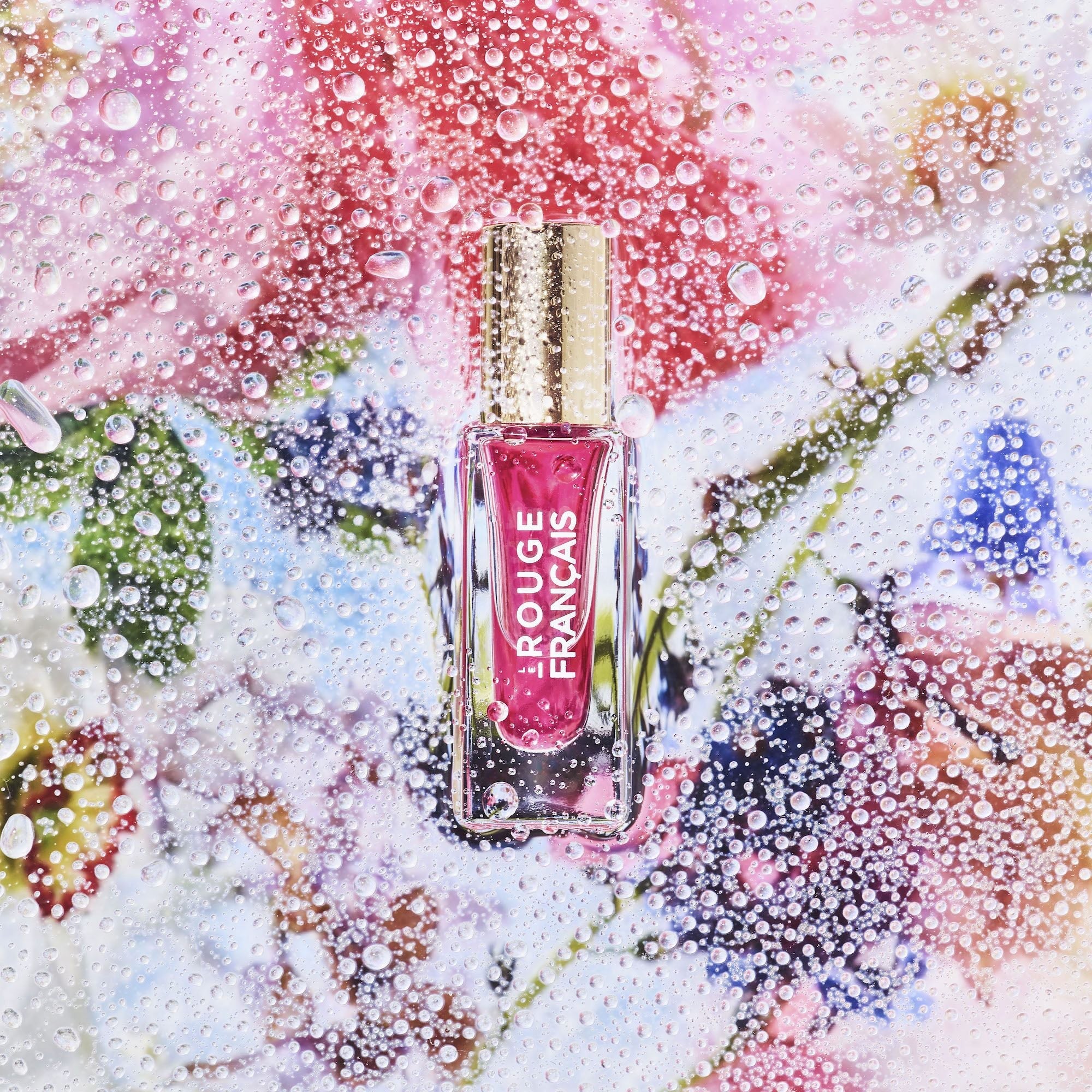 Le Rouge Francais Le Nectar No 614 Artemis Glasflasche vor buntem Hintergrund mit Wassertropfen.