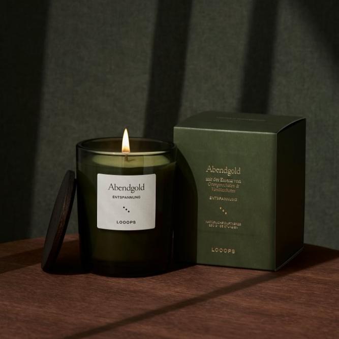 Tannengrünes Kerzenglas "Abendgold", daneben Deckel und Produktverpackung auf braunem Holzisch.